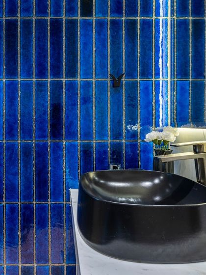 A close-up of the striking blue tiles in the Filigree House bathroom. The texture and deep color of the tiles, paired with a modern black sink, make a bold design statement.