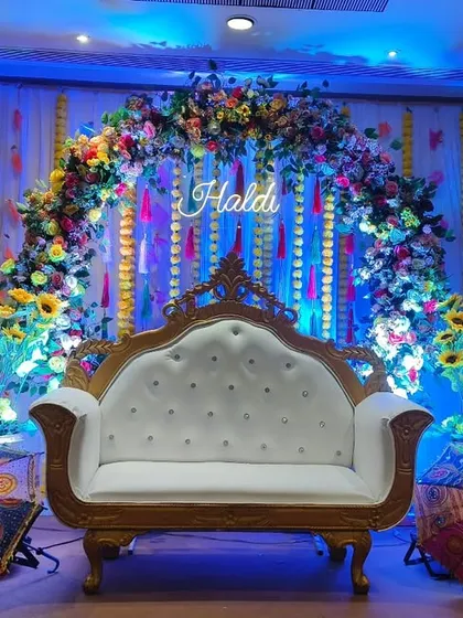 A grand and colorful Haldi stage. I used a floral arch with sunflowers, a royal white sofa, and decorative Rajasthani umbrellas to create a festive look.