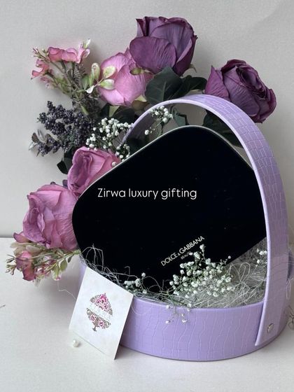 A heart-shaped basket in a lovely lavender shade, curated to hold a Dolce & Gabbana gift. The purple flowers and delicate baby's breath complete the look.