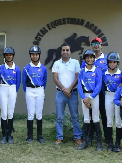 Our team posing in front of the REA logo. We are a diverse group of riders and coaches united by our love for horses and the pursuit of equestrian excellence.