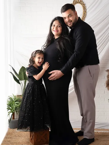 A sweet hug for the baby bump from the big sister-to-be. Dressed in matching black, this family portrait is both elegant and full of love.