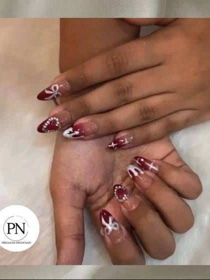 A festive design featuring deep red polish with white bow art and star details, perfect for the holiday season.
