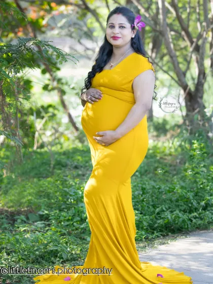 A profile view showcasing the beautiful silhouette of pregnancy. The mom-to-be cradles her bump in a fitted yellow gown, set against a soft, green natural background.