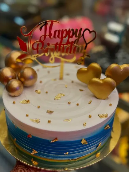 A birthday cake designed to make someone feel truly special. This creation features a beautiful blue and white gradient, adorned with golden hearts, spheres, and delicate gold leaf flakes, all topped with an elegant 'Happy Birthday' sign. I can create a similar masterpiece for your next celebration.