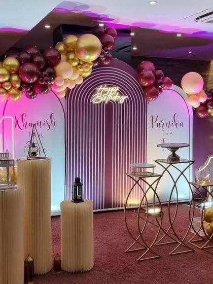 An elegant 10th birthday setup with a 'Happy Birthday' neon sign and a sophisticated maroon and rose gold balloon arrangement.