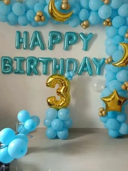 A simple and sweet 3rd birthday setup at home with a blue balloon arch and gold moon and star accents.