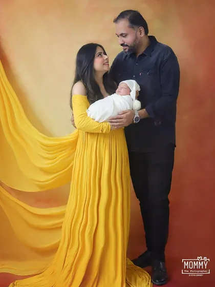 A classic family portrait with a new mom and dad looking at each other while holding their baby. The flowing yellow dress adds a beautiful touch of elegance and color to the photo.