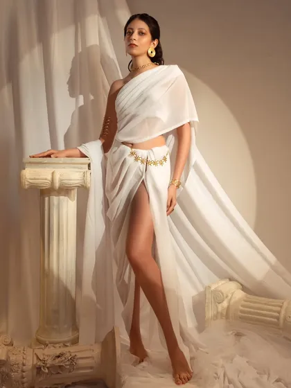 Inspired by Grecian goddesses, this shoot uses flowing white drapes and classical pillars to create a mythological scene. The high-slit drape and gold jewelry add a modern, powerful feel to the ancient aesthetic.