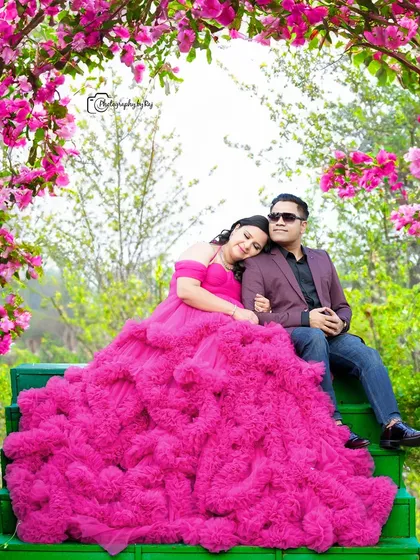 A romantic couple's portrait on green steps, surrounded by pink flowers. The mother-to-be's pink ruffled gown is simply breathtaking.