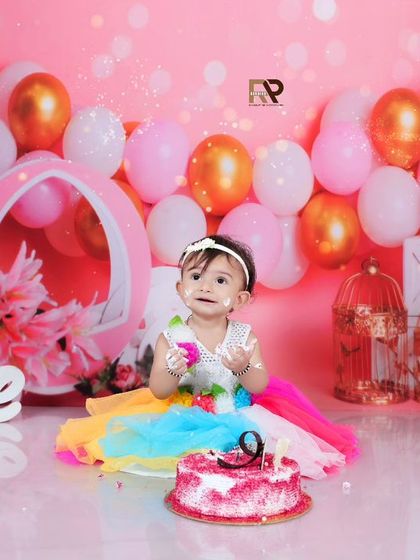 The cake smash is underway! This little girl enjoys her pink cake in a colorful dress, surrounded by festive pink and gold balloons.
