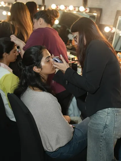 The bustling backstage area at a fashion show, with our artists working diligently to get models ready. This is the real-world environment our students thrive in.