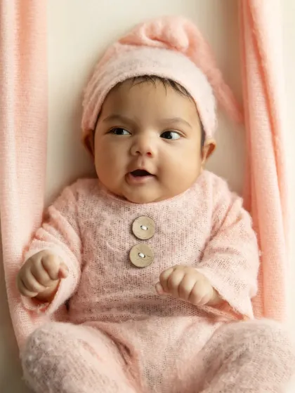 A close-up portrait of the baby in the pink swing, looking around with wide-eyed wonder.