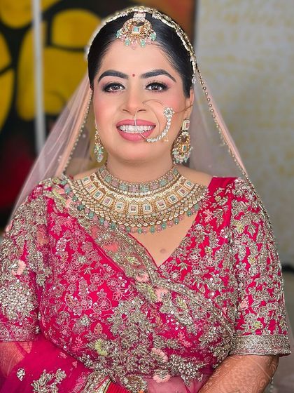 A happy bride in a pink lehenga, her smile is infectious. The makeup is fresh and glowing, with a focus on rosy cheeks and bright eyes.