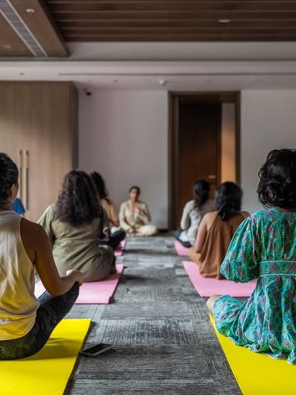 A view from the back of a wellness session, showing a community of individuals gathered to practice mindfulness together. The natural light and serene setting create a welcoming space for all levels of experience.