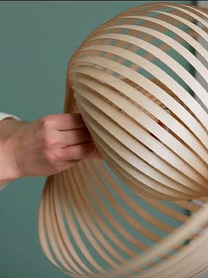A craftsperson's hands are seen assembling an Adilo lamp, showcasing the hands-on process and skill required to create these sustainable and timeless wooden lighting fixtures.