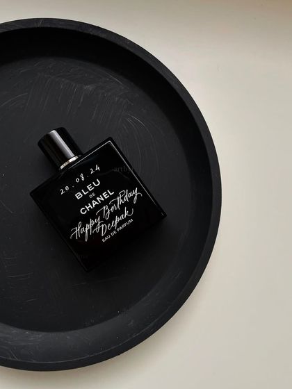 A styled shot of the engraved Bleu de Chanel bottle on a simple black tray. The clean, crisp white engraving stands out perfectly against the dark bottle.