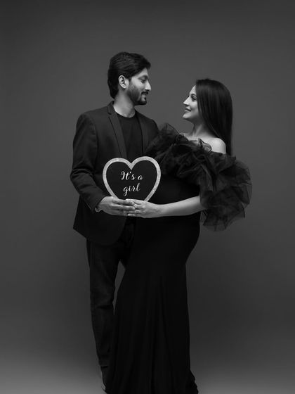 A beautiful black and white portrait for a gender reveal, holding a heart-shaped sign that says "It's a girl."