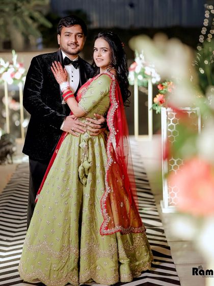 A classic engagement portrait of a couple in a beautifully decorated venue. The bride's light green and red lehenga contrasts wonderfully with the groom's black tuxedo.