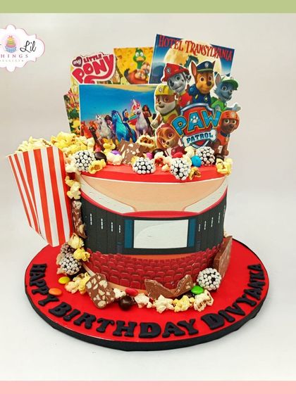 A movie night-themed cake perfect for Divyanshi's birthday, featuring popcorn, a film screen, and posters of her favorite shows like Paw Patrol and My Little Pony.