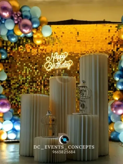 A detailed look at a modern birthday photo booth, showing the shimmering gold sequin wall, custom neon sign, and stylish cylindrical pedestals for cakes or decor.