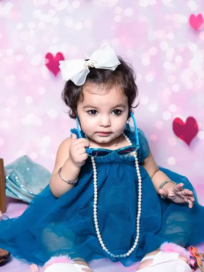A stylish portrait of a baby girl in a lovely blue dress. The string of pearls and oversized bow add a touch of playful elegance to her photoshoot.