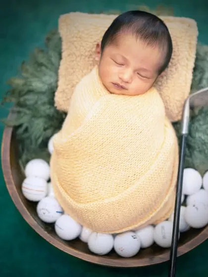 A future pro golfer in the making. This newborn is sleeping soundly on a bed of golf balls with a tiny club.
