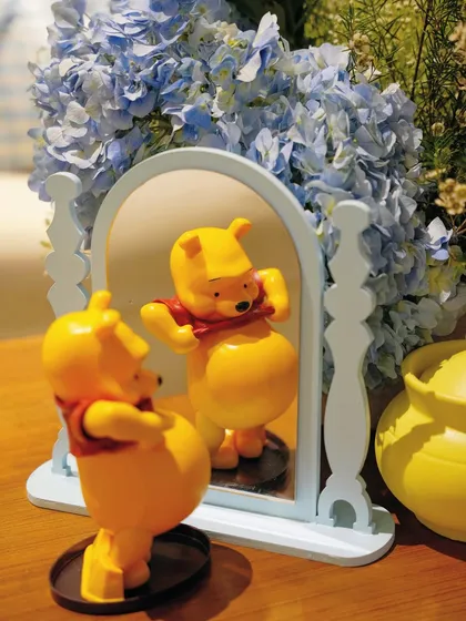 A charming detail of a Winnie the Pooh figurine looking in a mirror, placed alongside a "hunny" pot and fresh flowers.