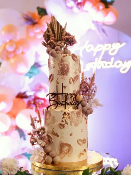 This two-tiered boho birthday cake combines textured buttercream in neutral tones with dried florals and edible chocolate spheres. It's a perfect example of rustic elegance for a stylish celebration.