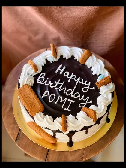 A round Lotus Biscoff cake with a chocolate drip and whipped cream swirls.