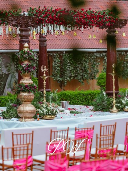 A detailed view of our traditional mandap setup, featuring stacked brass pots (kalash) with floral arrangements, polished wooden pillars, and a canopy of red roses.