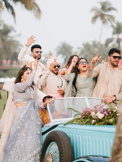 The groom and his friends make a stylish entry in a vintage blue car, waving and smiling, ready for the celebration.