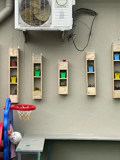 A simple yet effective vertical planter solution for a children's play area. These wooden shelves hold colorful pots, adding a playful touch of nature at a height that is both safe and visually appealing.