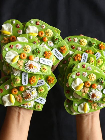 Holding two handfuls of personalized banana leaf meal magnets, ready to be shipped out for a wedding.