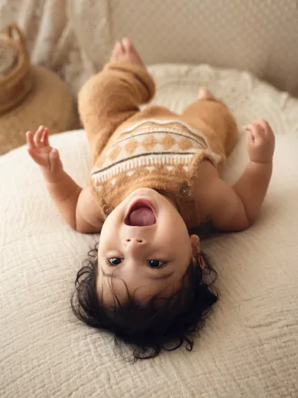 A happy baby in a cozy knit outfit lies upside down, giggling with pure delight. This is a perfect example of a fun and natural sitter session, capturing your baby's budding personality.