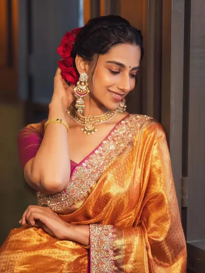 This shot highlights the beauty of traditional hairstyling with fresh flowers, paired with a shimmering golden-orange saree and classic temple jewelry. It’s a celebration of heritage.