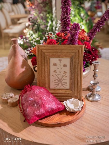 A curated collection of favors and decor, including a framed print, a potli bag, and terracotta vases, all reflecting the event's traditional yet chic aesthetic.