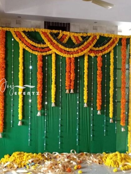 This backdrop for a half saree ceremony features a dark green fabric with hanging garlands of yellow and orange marigolds. We added strings of pearls and small bells for a delicate and festive look.