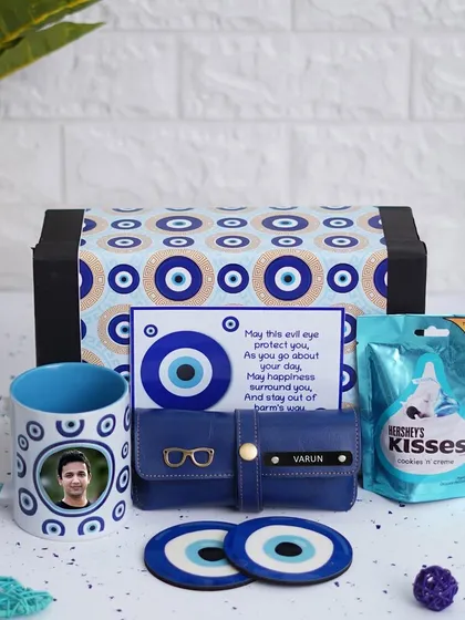 The Evil Eye Hamper is designed to bring good vibes. It includes a personalized mug, an evil eye themed eyewear case, matching coasters, and Hershey's Kisses chocolate.