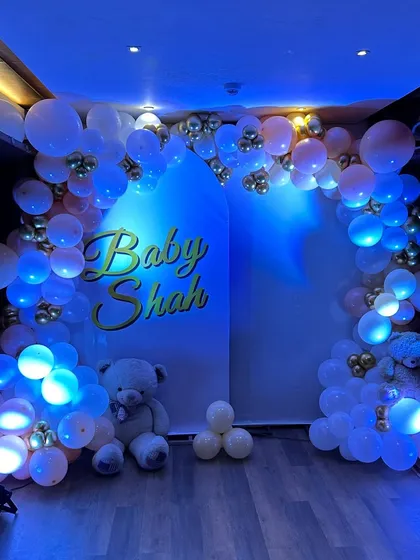 A beautiful baby shower backdrop with an arch of blue-lit balloons, creating a magical and ethereal glow for an evening celebration.