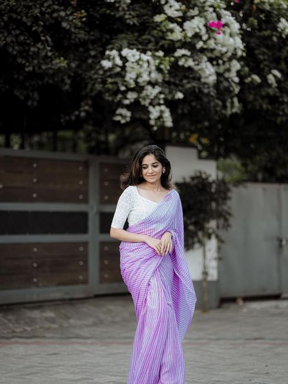 A full-length shot showing the graceful drape of the saree against a natural, leafy backdrop. This is a classic and timeless portrait style.