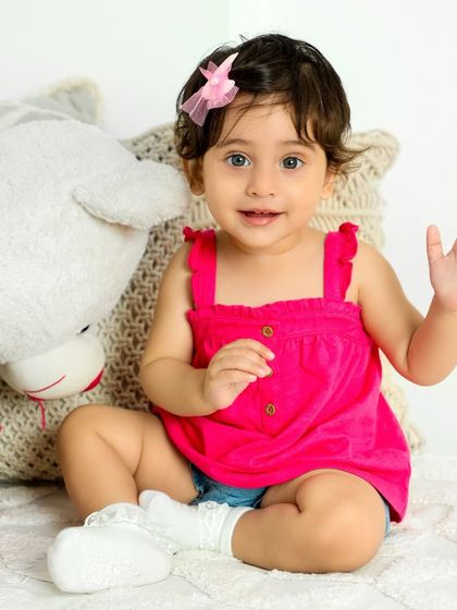 A sweet wave from this little girl in a bright pink top. Her friendly gesture and happy eyes make for an engaging portrait.