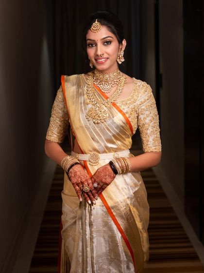 A full-length portrait of Hima in her gold tissue Kanjeevaram saree and hand-embroidered blouse, a perfect ensemble for a modern South Indian bride.