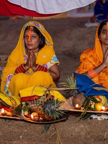 Two women offer prayers with their 'soop' filled with fruits and offerings for the Sun God. This shot details the specific rituals and materials central to the Chhath festival.