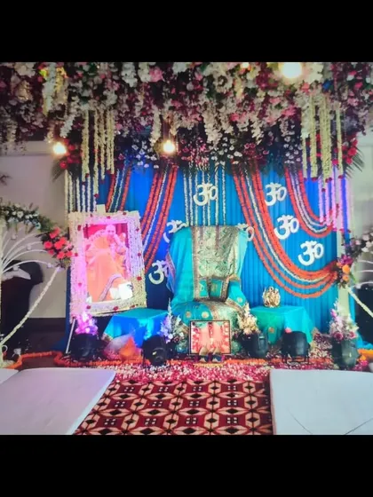 This Guruji Satsang stage decoration was designed with a vibrant blue color theme as requested by the client. The setup includes a floral canopy, a draped backdrop with marigold 'Om' symbols, and a decorated Aasan.