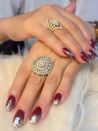 A dramatic and festive look with deep maroon nails and a silver glitter ombre. The large, chunky rings show just how well a great manicure can accessorize.