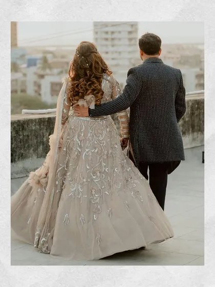 A classic walking shot from behind, highlighting the beautiful details of the bride's lehenga and the couple's connection.