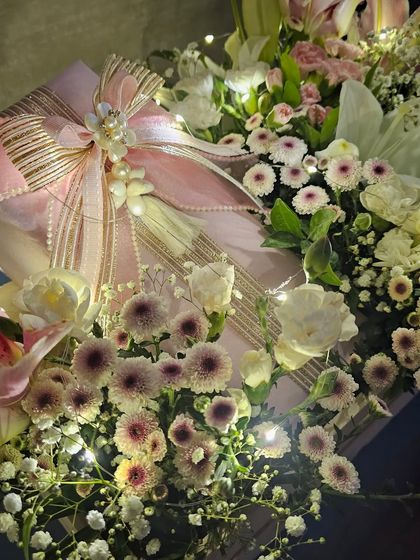 A close-up of the bow and tassel detail on a gift from a pink floral trousseau. The combination of shimmering ribbon, pearls, and soft lighting creates a look of pure elegance and romance.