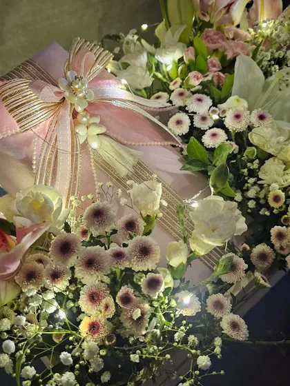 A close-up of the bow and tassel detail on a gift from a pink floral trousseau. The combination of shimmering ribbon, pearls, and soft lighting creates a look of pure elegance and romance.