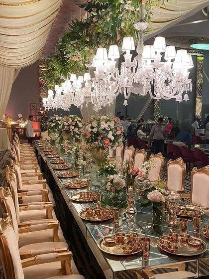 Dining is an experience, and I design every detail to make it extraordinary. This grand sangeet dinner setup features a long, mirrored table reflecting a cascade of magnificent chandeliers, surrounded by elegant seating and lush floral arrangements for a truly luxurious feel.