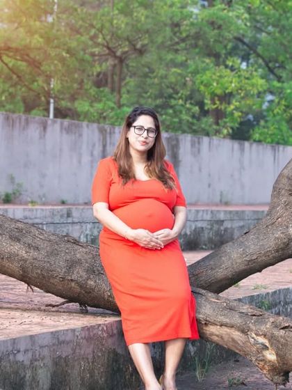 A simple and contemplative moment. This mom-to-be sits on a fallen tree, cradling her bump in a comfortable red dress, lost in thought about the future.